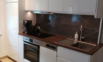 A modern kitchen with white cabinets and wooden surfaces. The equipment includes a stove, an oven, and a coffee machine.
