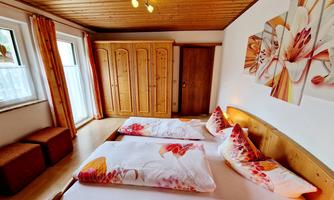 A cozy bedroom with two beds and colorful cushions. The room has wooden paneling and large windows that let in plenty of light.