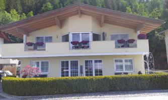 A beautiful house with a large roof and balconies. The windows are decorated with colorful flowers and a green hedge surrounds the property.