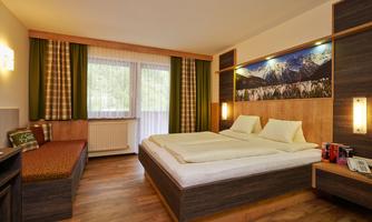 A modern furnished bedroom with two beds and a cozy sitting area. Large windows provide plenty of daylight and offer a view of nature.