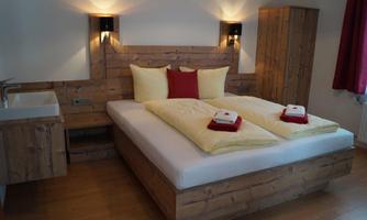 A modern bedroom with a large bed and wooden details. The walls are light, and there is soft lighting as well as decorative pillows.