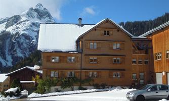 A rustic wooden house in the snow with a view of the mountains. The surroundings are wintry and picturesque with snowy landscapes.