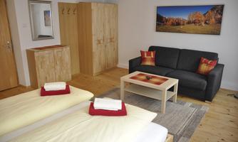 A cozy room with two beds, a sofa, and a table. On the wall hangs a picture of an autumn landscape.