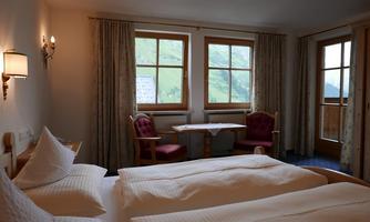 A cozy hotel room with two beds and a table. Large windows offer a view of the green countryside outside.
