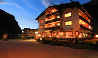 A charming hotel with illuminated windows at dusk. The surrounding mountains provide a picturesque backdrop.