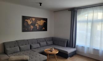 A modern living room with a gray sofa and a round table. A world map hangs on the wall and the window lets in a lot of light.
