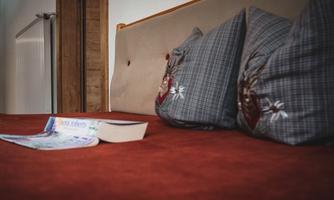 A cozy bed with padded pillows and a warm blanket. On it lies an open book and a magazine.