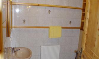 A simple bathroom with bright tiles and wooden walls. It includes a toilet, a sink, and towels.
