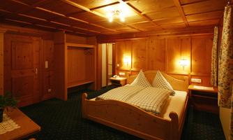 A cozy bedroom with wooden paneling and a double bed. There is a clothing rack and soft lighting.