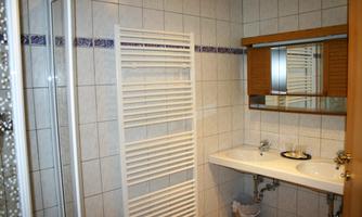A modern bathroom with tiled walls and a mirror above the sink. There is a shower and a towel rack.