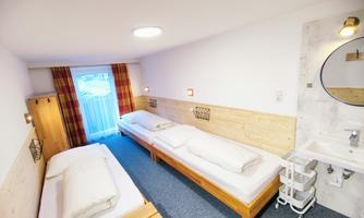 A simple room with two beds and a small sink. Large windows provide plenty of daylight.