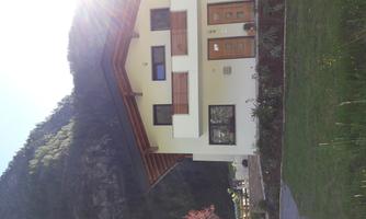 A modern two-story house with a wooden roof. In the background, green mountains and a clear sky are visible.