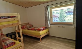 A simple bedroom with a bunk bed and a single bed. A window offers a view of the surrounding scenery.