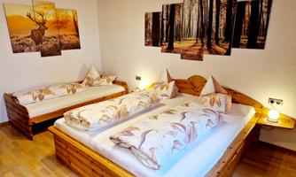 A cozy bedroom with two wooden beds and matching pillows. On the wall, pictures of forests and a deer are hanging.