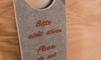 A hanging sign with the inscription "Bitte nicht stören" and "Please do not disturb." It hangs on a door with a silver door handle.