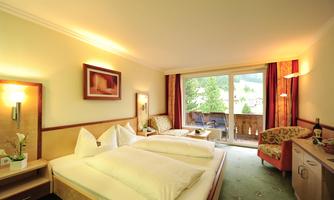 A beautiful hotel room with two single beds and a balcony. The room is bright and cozy, with floral decor and a view of greenery.