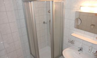 A modern bathroom with a shower stall and a sink. The walls are tiled with white tiles.
