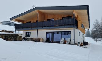 A modern house with a covered balcony in a snow-covered landscape. The surroundings are calm and idyllic, perfect for winter sports.