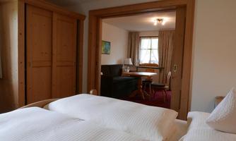 A cozy bedroom with a double bed and a wardrobe. In the background, a spacious living area with a table and a seating area can be seen.