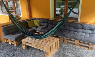 A cozy outdoor seating area with gray cushions and a hammock. The table is made from pallets and the walls are painted in a warm orange.