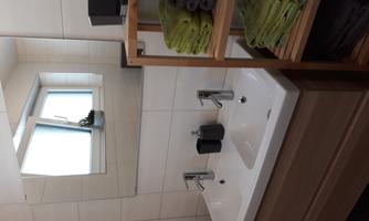 A modern bathroom with two sinks and a large mirror. Towels in various colors are stored on a shelf.