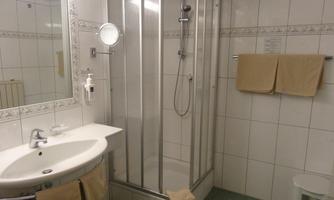 A modern bathroom with a shower and a sink. Wall tiles in bright white and a small stool complement the decor.