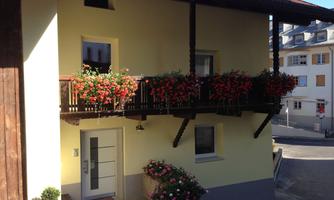 A pretty house with a balcony decorated with colorful flowers. The facade is yellow and there are modern windows.