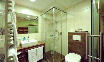 A modern bathroom featuring a rain shower, a white sink, and wooden details. Towels are neatly hung, and the space is bright and inviting.