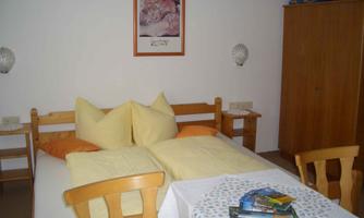 A cozy bedroom with a double bed and two pillows. On the table, there are some brochures and a picture hangs on the wall.