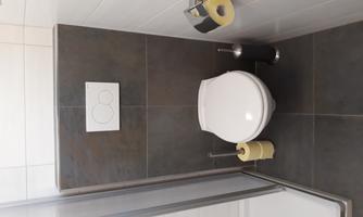 A modern bathroom with a toilet and a sink. On the wall, there are two holders for toilet paper, and a shower cubicle is visible in the background.