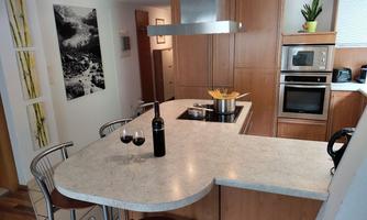 A modern kitchen with a spacious kitchen island and bar stools. On the countertop, there is a pot of pasta and a bottle of red wine next to two wine glasses.