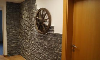 A modern entrance area with a stone wall and a decorative ship's wheel. The warm wooden tones of the door complement the cool stone pattern.