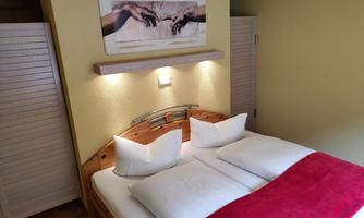 A cozy bedroom with a double bed and red cushions. A piece of art with a famous motif hangs on the wall.