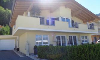 A modern house with a large balcony and a bright yellow paint. The garden is well-maintained and offers a pleasant atmosphere.