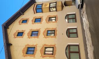 A historic building with decorative windows and intricate facade elements. The facade is in soft colors and is located on a quiet street.
