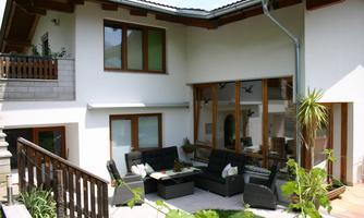 A modern terrace with comfortable garden furniture and a large window front. Surrounded by plants and a bright, inviting atmosphere.