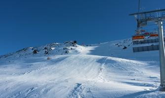A snow-covered slope under a clear blue sky. In the background, a ski lift can be seen.