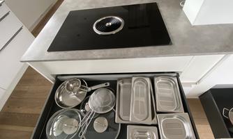 A modern kitchen drawer with various pots and lids. The surface is made of elegant gray material.