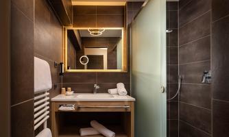A modern bathroom with an elegant shower and a wooden washbasin. The walls are in dark shades, and a large mirror provides brightness.