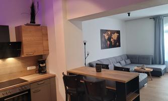 A modern apartment with an open kitchen and a cozy living room. The living room is bright and features a gray couch and a world map on the wall.