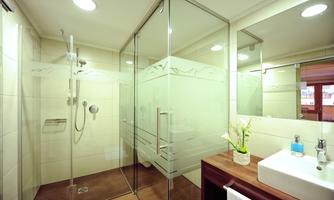 A modern bathroom with a glass shower cabin and light wooden flooring. Decorative accessories are placed on the sink.