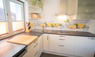 Modern kitchen with bright furniture and a colorful wall decoration of fruits. A wooden countertop and natural light sources create an inviting atmosphere.