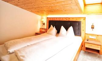 A cozy bedroom with a large double bed and two pillows. Wooden paneling and warm light create an inviting atmosphere.