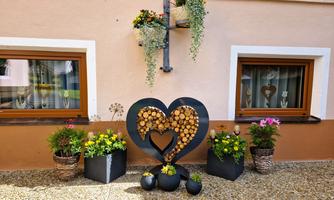 A cozy corner of the house with two windows and colorful flowers in pots. In the foreground is a large heart made of wooden slices.