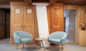 A cozy room with two light blue armchairs and a small table in the center. Surrounded by wooden walls and cabinets, the room conveys a relaxed atmosphere.