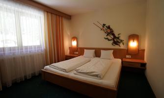 A simple bedroom with a double bed and two pillows. The room is bright and cozy, with curtains and soft lighting.
