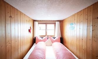 A cozy bedroom with wooden paneling and a double bed. The red pillows and curtains create a warm and inviting look.