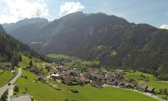 A picturesque mountain landscape with a small village in the valley. Surrounded by green meadows and high mountains under a clear sky.