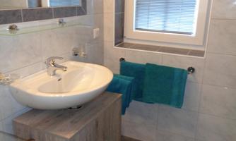 A modern bathroom with a sink and wooden cabinet. There are towels in turquoise and a window with blinds.