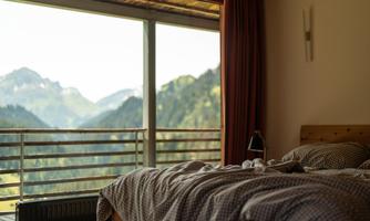 A cozy bedroom with a bed and a view of the mountains. Large windows offer a view of the green mountain landscape.
